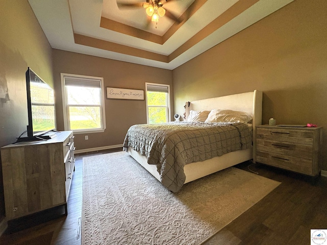 bedroom featuring dark wood-style flooring, a tray ceiling, baseboards, and a ceiling fan