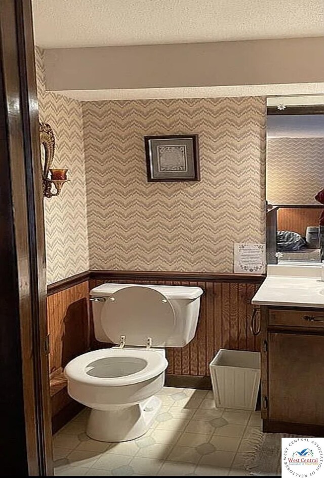592 Woodland Dr, Climax Springs, MO 65324 - half bath with wallpapered walls, a textured ceiling, toilet, wainscoting, and tile patterned floors