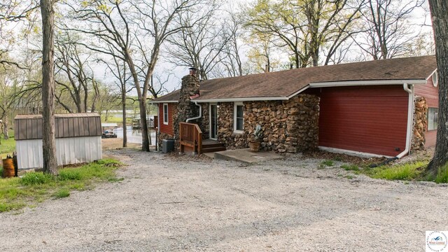 exterior space with an outdoor structure, a shed, stone siding, and a chimney