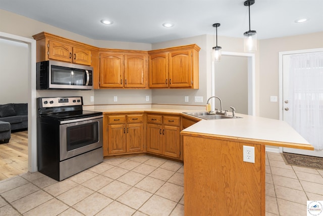 kitchen featuring hanging light fixtures, appliances with stainless steel finishes, light countertops, a sink, and a peninsula
