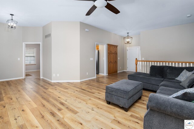 living room with lofted ceiling, visible vents, light wood finished floors, and ceiling fan with notable chandelier