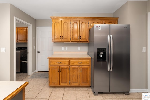 kitchen featuring light tile patterned floors, stainless steel fridge with ice dispenser, light countertops, baseboards, and washer / clothes dryer