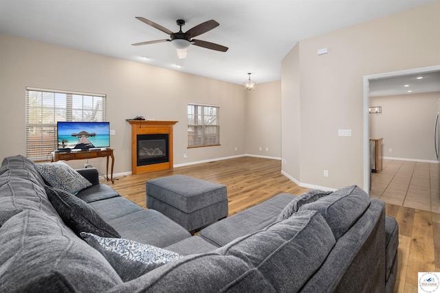 living room featuring baseboards, ceiling fan, and light wood finished floors