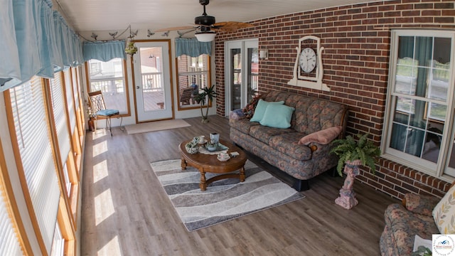 living room with wood finished floors, brick wall, and a ceiling fan