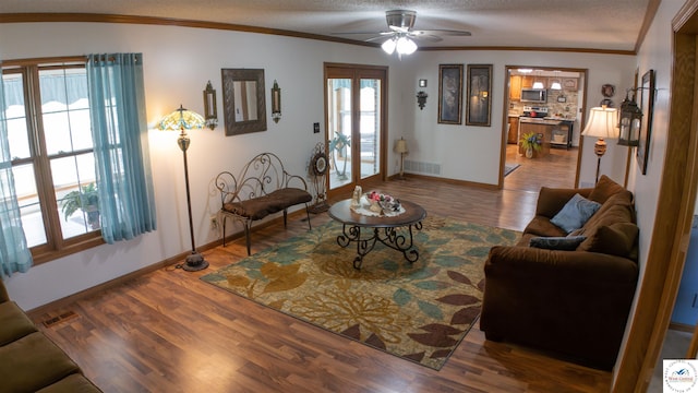 living area with a textured ceiling, visible vents, baseboards, wood finished floors, and a ceiling fan