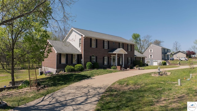 colonial inspired home with brick siding, curved driveway, a front lawn, and a residential view
