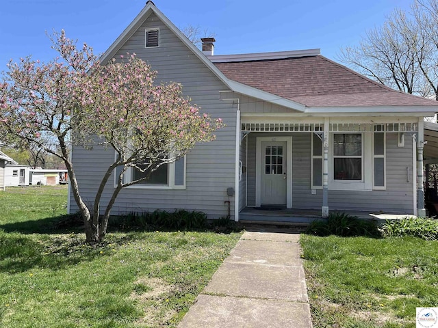 bungalow featuring roof with shingles, a chimney, a porch, and a front lawn