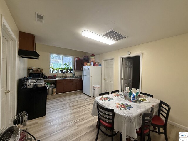 kitchen with stainless steel microwave, a sink, visible vents, freestanding refrigerator, and light wood-type flooring