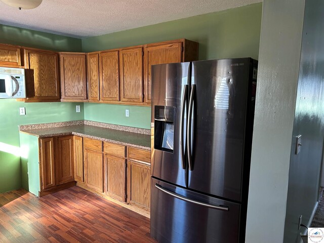 923 E Walnut St, Rich Hill, MO 64779 - kitchen featuring dark wood-type flooring, white microwave, brown cabinetry, and stainless steel fridge with ice dispenser