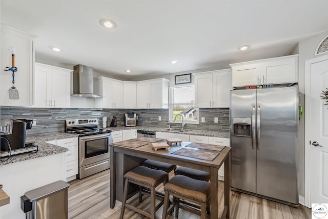 kitchen featuring stainless steel appliances, white cabinetry, a sink, and wall chimney exhaust hood