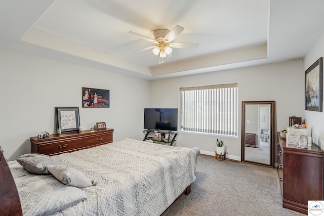 carpeted bedroom featuring a raised ceiling, baseboards, and a ceiling fan