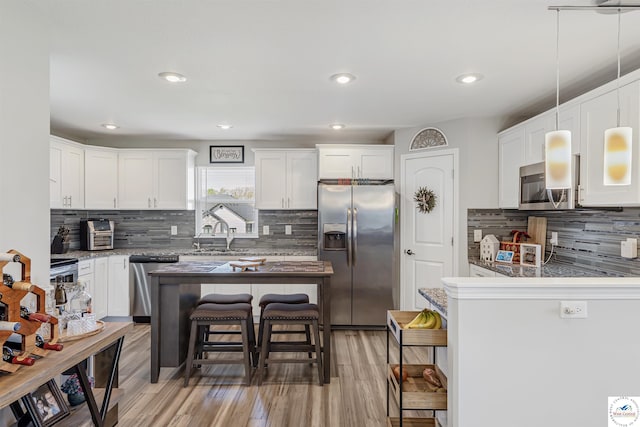 kitchen featuring a breakfast bar area, white cabinetry, tasteful backsplash, light wood-style flooring, and appliances with stainless steel finishes