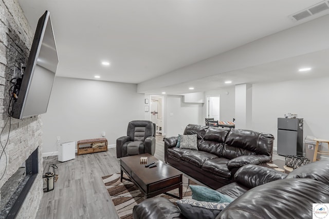 living room with light wood-type flooring, recessed lighting, a stone fireplace, and visible vents