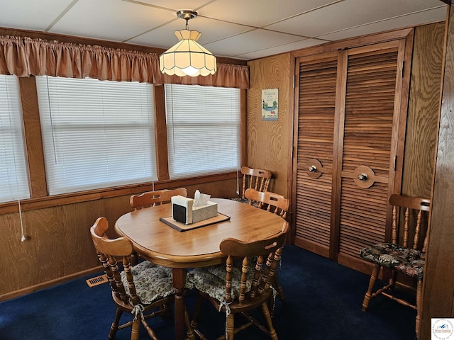 dining area with a drop ceiling, carpet flooring, wood walls, and visible vents