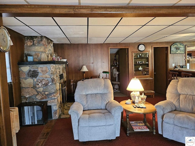 living room featuring a drop ceiling, built in features, carpet flooring, a fireplace, and wooden walls