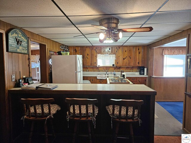 kitchen with carpet flooring, brown cabinets, wood walls, light countertops, and freestanding refrigerator