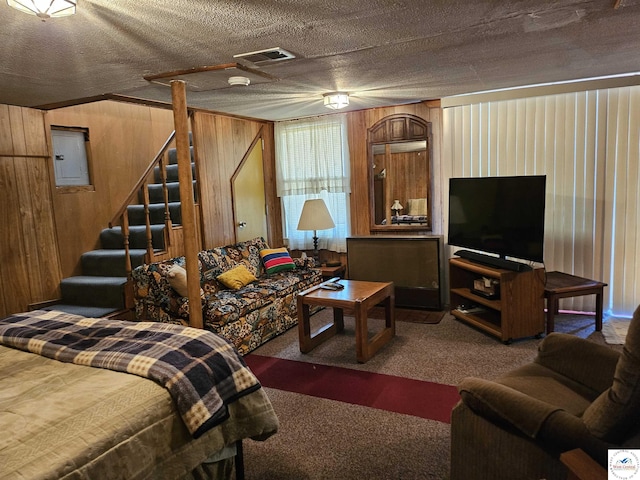living room featuring carpet flooring, visible vents, electric panel, wooden walls, and stairs