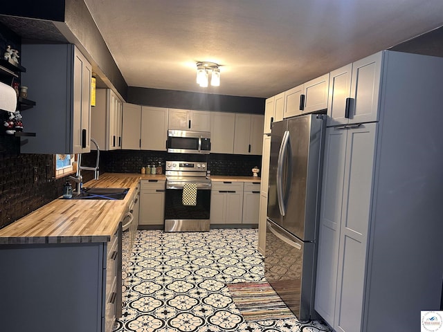 kitchen with a sink, decorative backsplash, stainless steel appliances, and butcher block countertops