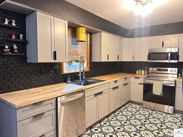 kitchen with white cabinets, a sink, butcher block countertops, stainless steel appliances, and tasteful backsplash