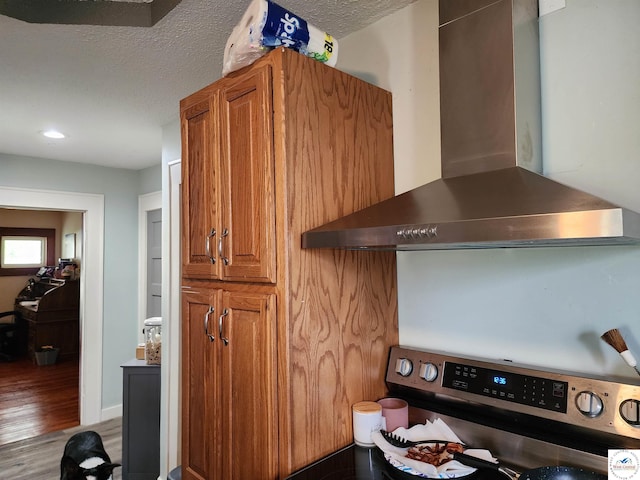 interior details featuring wood finished floors, wall chimney range hood, a textured ceiling, brown cabinets, and electric stove