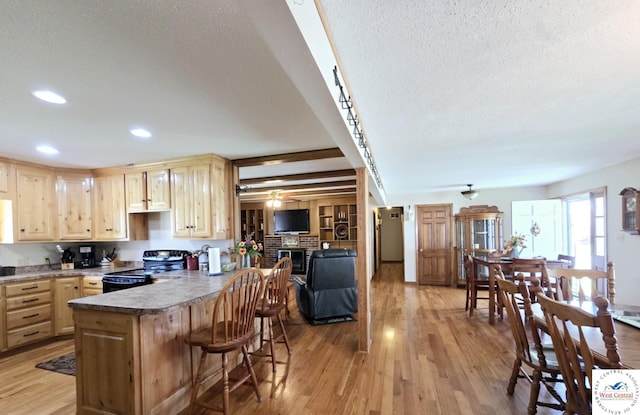 502 S Ferguson Ave, Tipton, MO 65081 - kitchen featuring a breakfast bar area, a textured ceiling, light brown cabinetry, stainless steel range with electric cooktop, and light wood finished floors
