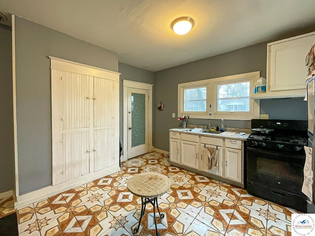 kitchen with light countertops, white cabinets, black gas stove, a sink, and baseboards