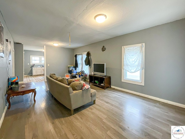living area featuring a textured ceiling, light wood-style floors, and baseboards