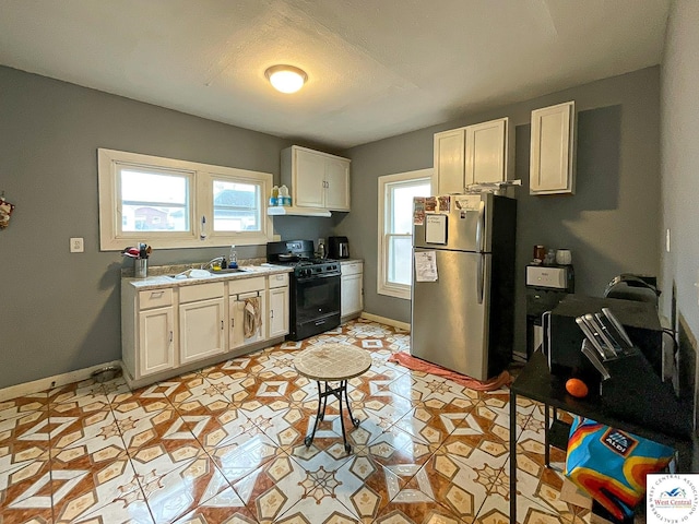 kitchen featuring a sink, a healthy amount of sunlight, freestanding refrigerator, and black gas range