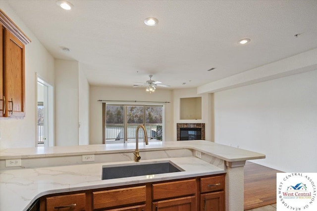 kitchen featuring a sink, ceiling fan, brown cabinets, and a glass covered fireplace