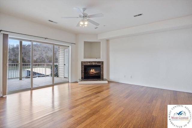 unfurnished living room with a premium fireplace, visible vents, ceiling fan, and light wood-type flooring