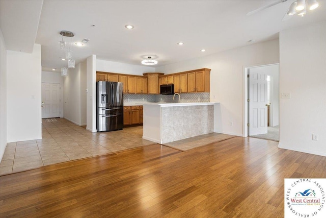 kitchen with light wood-style floors, black microwave, a peninsula, light countertops, and stainless steel fridge with ice dispenser