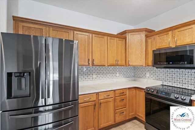 kitchen with light stone countertops, light tile patterned flooring, brown cabinetry, backsplash, and appliances with stainless steel finishes