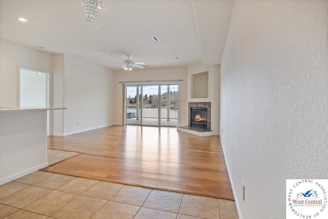 unfurnished living room with a textured wall, ceiling fan, a warm lit fireplace, and baseboards