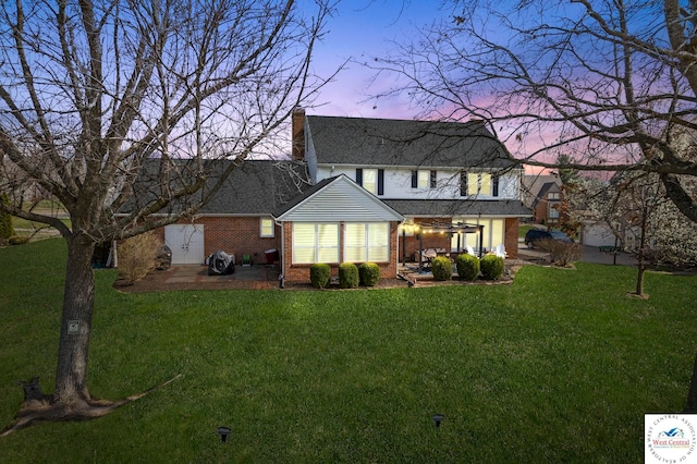 back of house featuring a lawn, roof with shingles, a patio area, and brick siding