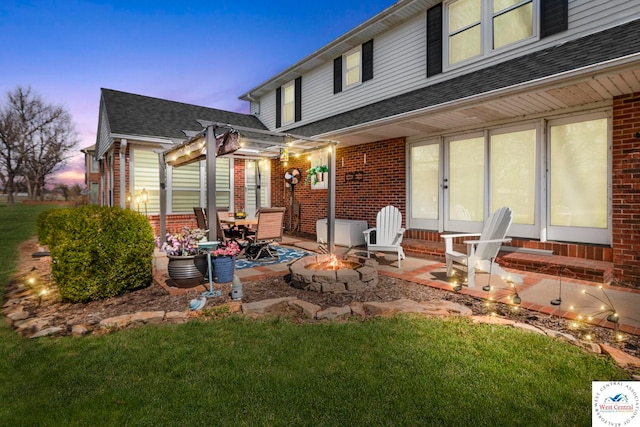 back of property at dusk featuring an outdoor fire pit, a patio area, a shingled roof, and brick siding