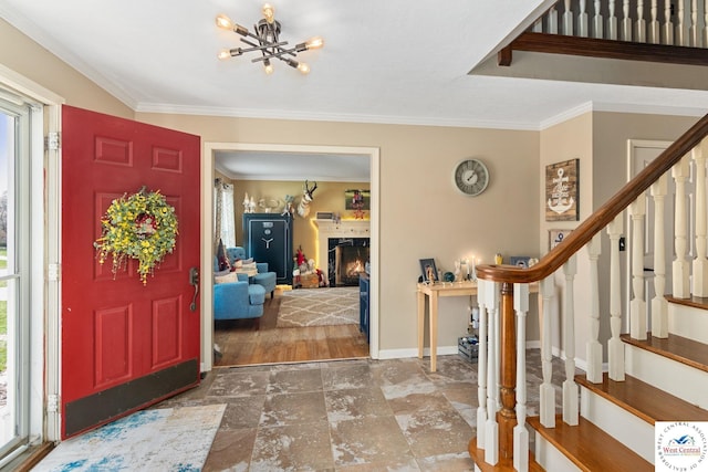 foyer featuring crown molding, a lit fireplace, baseboards, a notable chandelier, and stairs