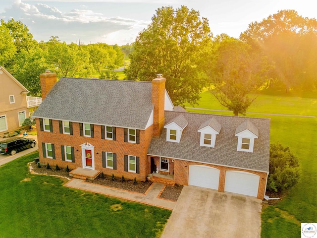 colonial-style house featuring a chimney, brick siding, a shingled roof, driveway, and a front lawn
