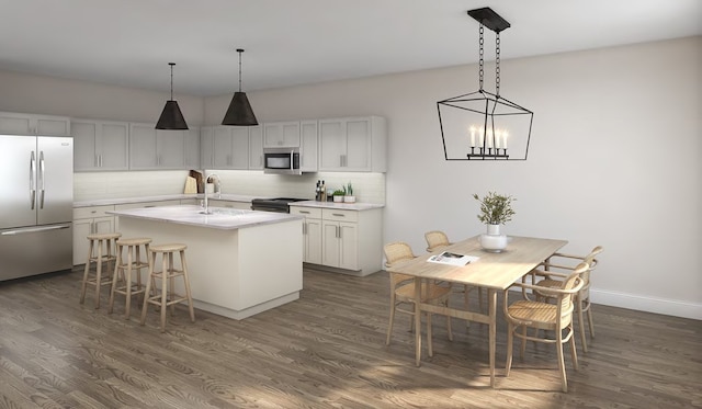 kitchen with dark wood-style flooring, light countertops, an island with sink, stainless steel appliances, and decorative backsplash