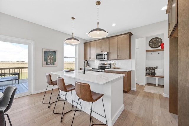 kitchen with appliances with stainless steel finishes, a kitchen island with sink, light hardwood / wood-style floors, and plenty of natural light