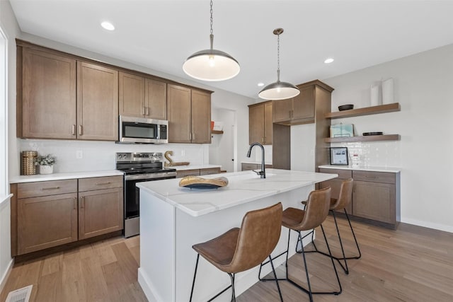 kitchen with decorative backsplash, an island with sink, light stone countertops, light hardwood / wood-style flooring, and stainless steel appliances