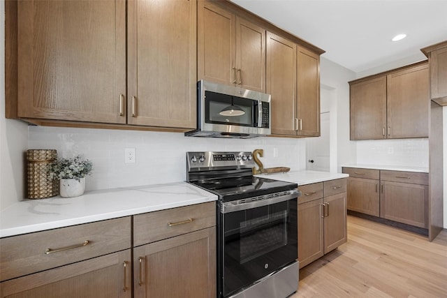 kitchen with light stone counters, tasteful backsplash, stainless steel appliances, and light wood-type flooring