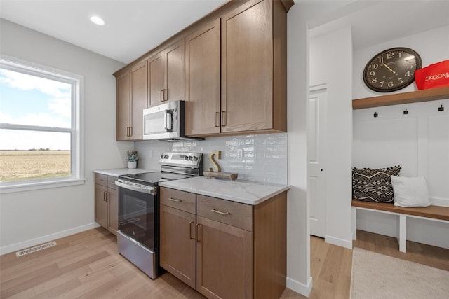 kitchen with light hardwood / wood-style floors, decorative backsplash, light stone countertops, and stainless steel appliances