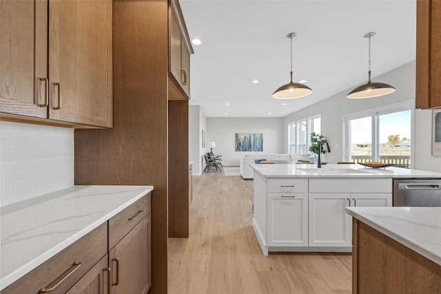 kitchen with white cabinets, hanging light fixtures, stainless steel dishwasher, light hardwood / wood-style flooring, and sink