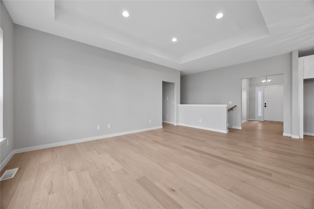 spare room with a tray ceiling and light wood-type flooring