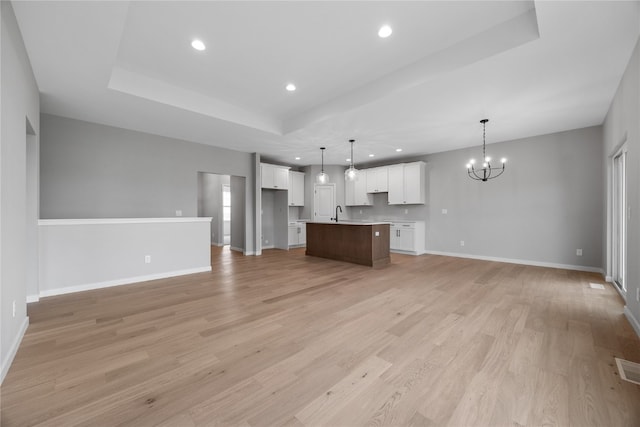 kitchen featuring light wood-type flooring, an island with sink, decorative light fixtures, white cabinets, and a chandelier