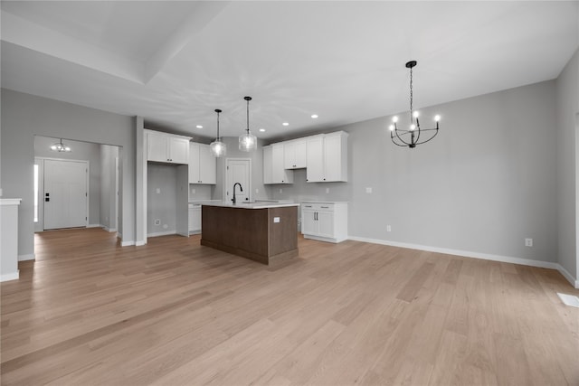 kitchen with an island with sink, white cabinetry, a chandelier, light wood-type flooring, and decorative light fixtures