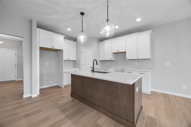 kitchen with light hardwood / wood-style floors, white cabinets, hanging light fixtures, and a center island with sink