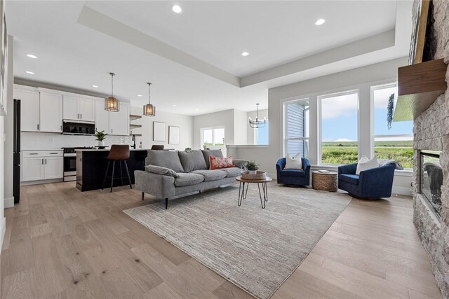 living room with light wood-type flooring, a raised ceiling, and a stone fireplace