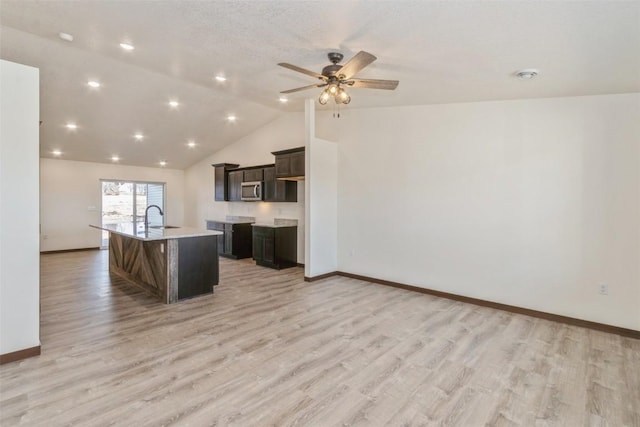 kitchen with stainless steel microwave, a center island with sink, light wood-type flooring, light countertops, and a sink