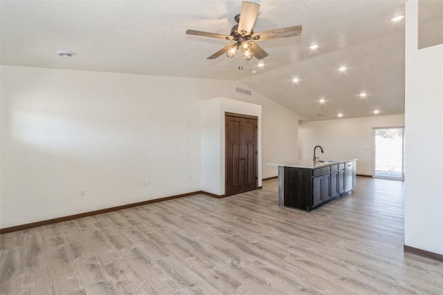 kitchen featuring visible vents, an island with sink, a sink, vaulted ceiling, and light wood-style floors